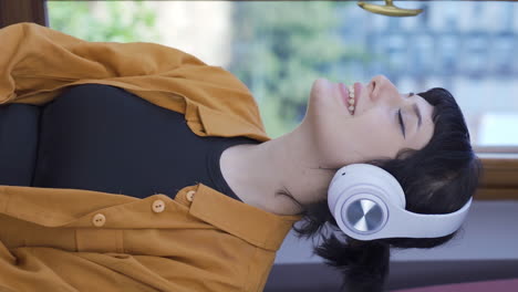 Vertical-video-of-Young-woman-looking-out-the-window-and-listening-to-music-with-headphones.